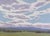 This oil painting captures a serene landscape under expansive blue skies, with soft, billowing clouds that evoke a sense...