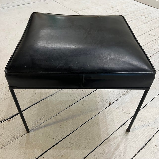 This is a black vinyl and iron ottoman designed by Paul McCobb. Perfect for a footrest, stool or extra seating.