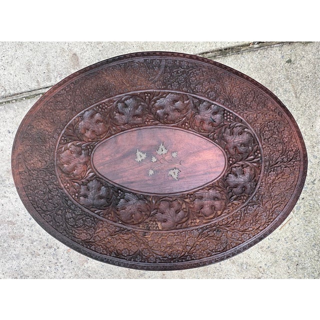 Anglo Indian Folding Table. Carved with vine leaves and brass inlay floral pattern. Oval top on an octagonal folding base.