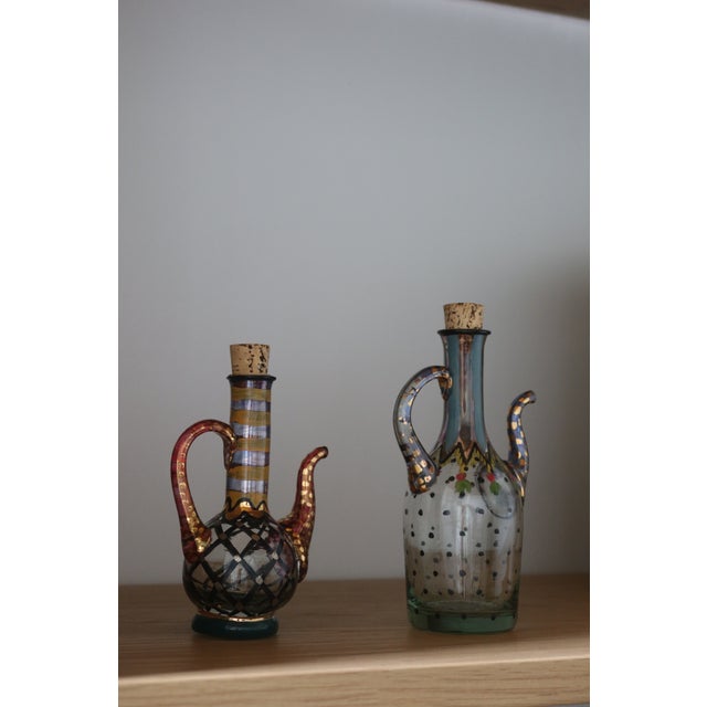 A rare and collectible pair of hand-painted glass cruets from the original Victoria & Richard MacKenzie-Childs era, both...