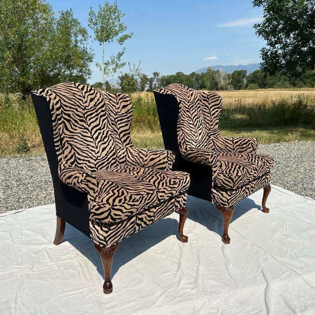 A striking pair of Queen Anne–style wingback chairs custom upholstered in a rich black on camel zebra print in soft...