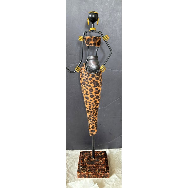 This vintage African-inspired handcrafted metal sculpture depicts a graceful female figure carrying a traditional vessel,...