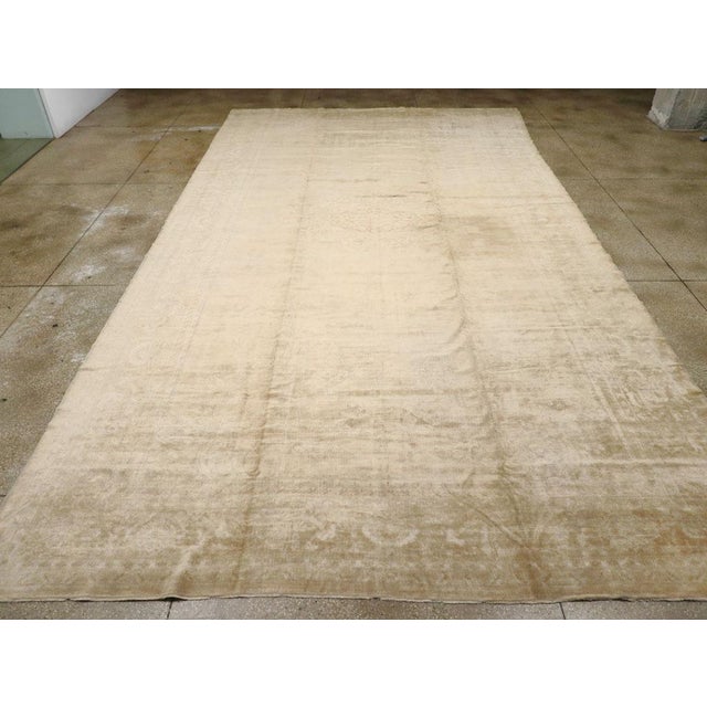 An antique Turkish Oushak oversize carpet. A round light brown medallion is freely placed on a beige ground in this...