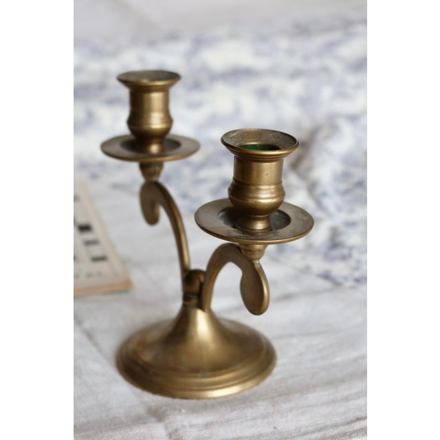 Elegant vintage two-armed candle holder in gilded brass, featuring a symmetrical, curved design. Its balanced silhouette...