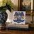 A classic Dutch Delft-style hand painted blue and white porcelain tile featuring an intricately rendered heraldic coat of...