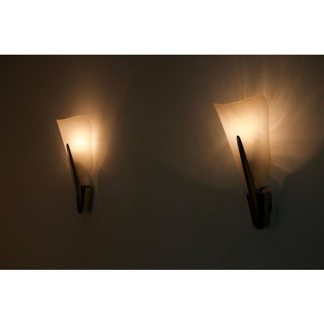 Elegant pair of italian wall lamps from the 1960s, combining sculptural brass fittings with softly curved, translucent...