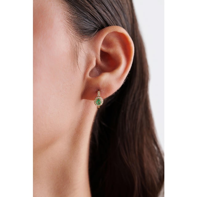 These elegant huggie hoop earrings feature a 0.36 ct natural oval-cut emerald, set in 14k yellow gold. accented by a...