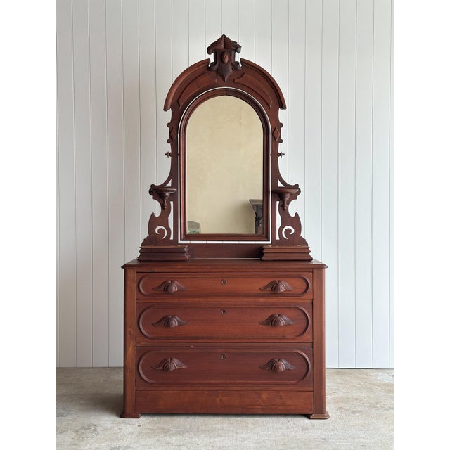 This antique wooden dresser features an impressive arched mirror, sculpted drawer pulls, three generous drawers, and a...