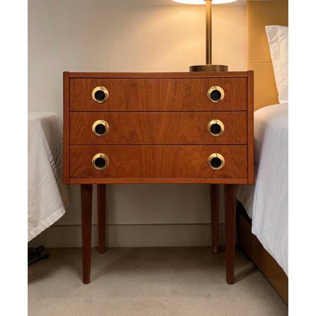 Petite teak nightstand produced by a danish cabinetmaker. compact three-drawer construction raised on tapered legs,...