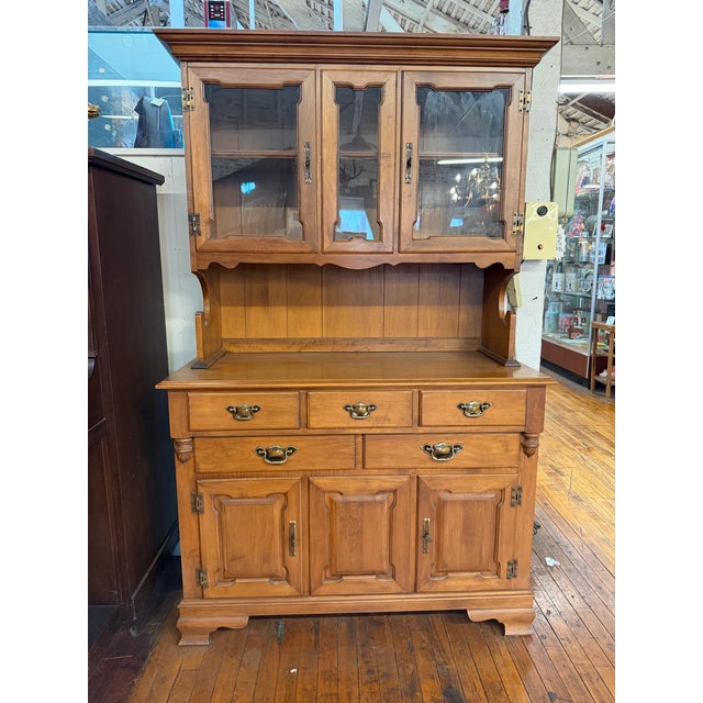 Traditional wooden china hutch featuring glass-paneled upper cabinets, decorative brass-tone hardware, and generous drawer...