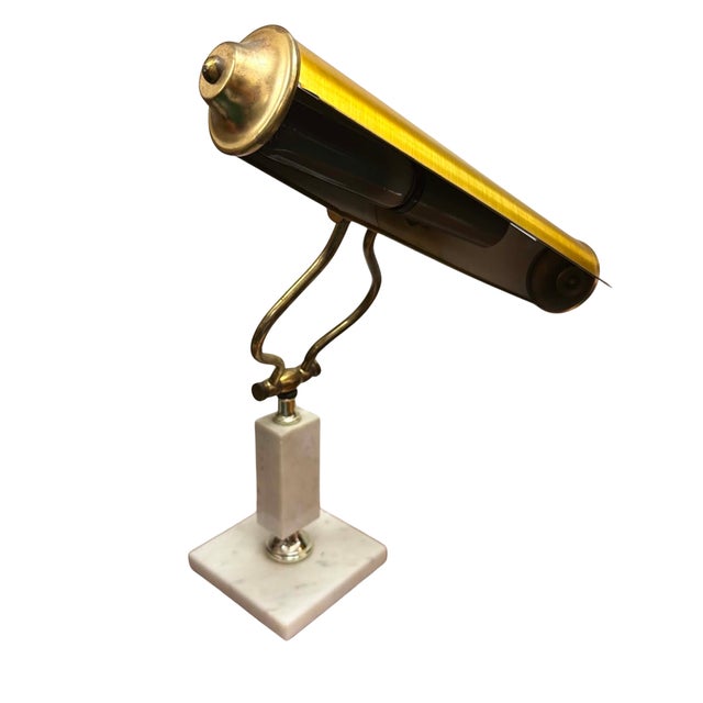 A vintage piano lamp featuring a classic elongated brass shade designed to provide even illumination for sheet music,...