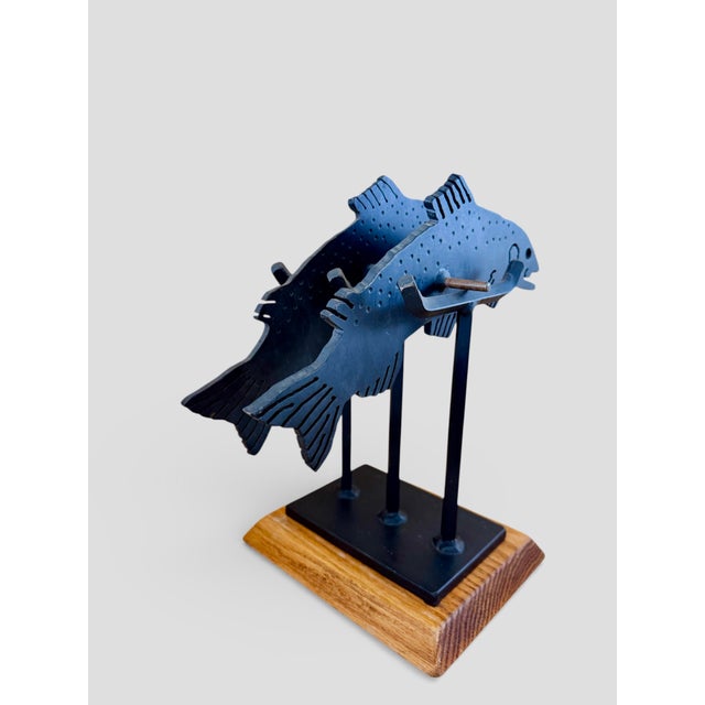 A signed kinetic sculpture handcrafted by Charles Ringer in 1994 titled "Trout", featuring two stylized trout on a riser,...