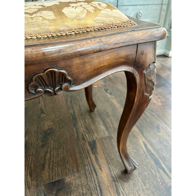 Charming Louis XV–style upholstered stool featuring a carved wood frame with cabriole legs and shell motif. The padded...
