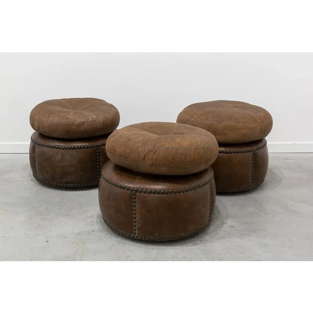 Round poufs with four wheels each made of brown studded leather.
