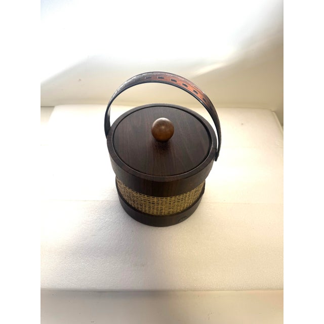 a vintage Mid-Century Modern (MCM) ice bucket, commonly featuring a faux wood grain finish with a rattan or wicker...