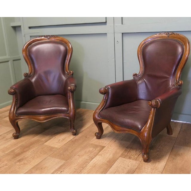 A Pair of Victorian Leather Spoon Back Easy Chairs. The chairs have solid carved mahogany frames, they are set on chunky...