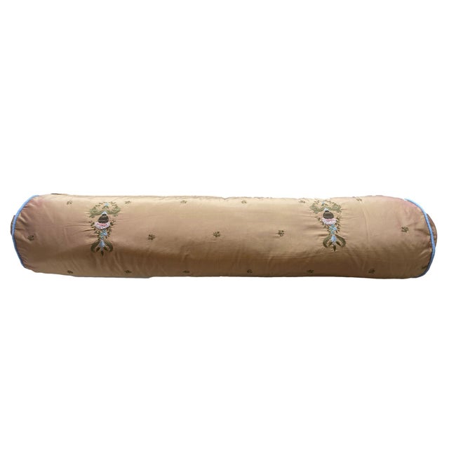 This bolster pillow features a reflective golden fabric with intricate floral and vine embroidery in muted green, blue,...