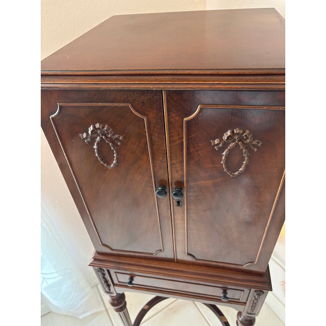 A tall mid‑century mahogany flatware cabinet on stand, featuring seven velvet‑lined drawers designed to hold a complete...