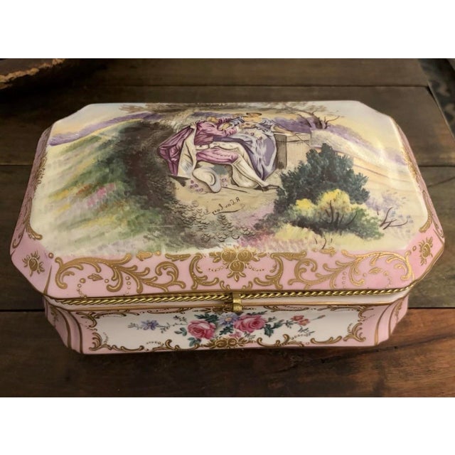 A porcelain bomb casket box featuring a hand painted Watteau style romantic scene on the lid, surrounded by pink and gilt...