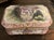 A porcelain bomb casket box featuring a hand painted Watteau style romantic scene on the lid, surrounded by pink and gilt...