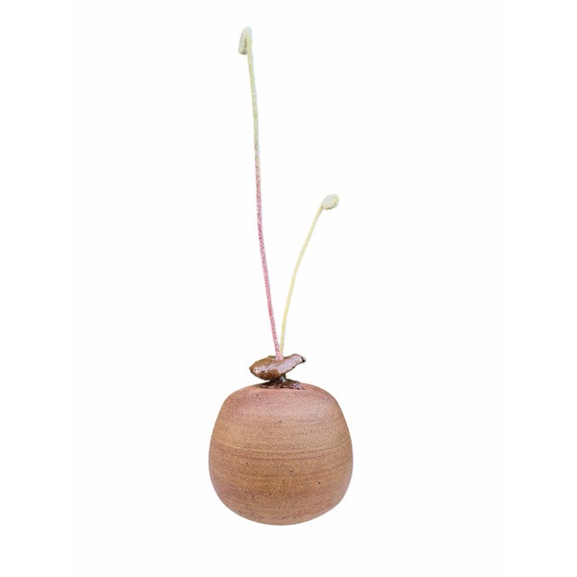 An organic mixed media decor sculpture featuring a hand-formed studio pottery vessel with integrated faux fiddlehead fern...