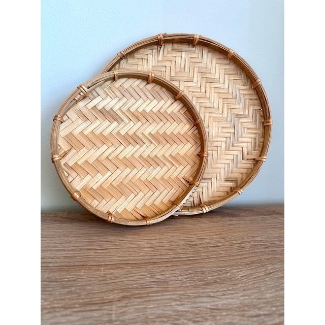 A charming pair of traditionally styled handwoven bamboo trays featuring intricate herringbone weaving, warm natural...