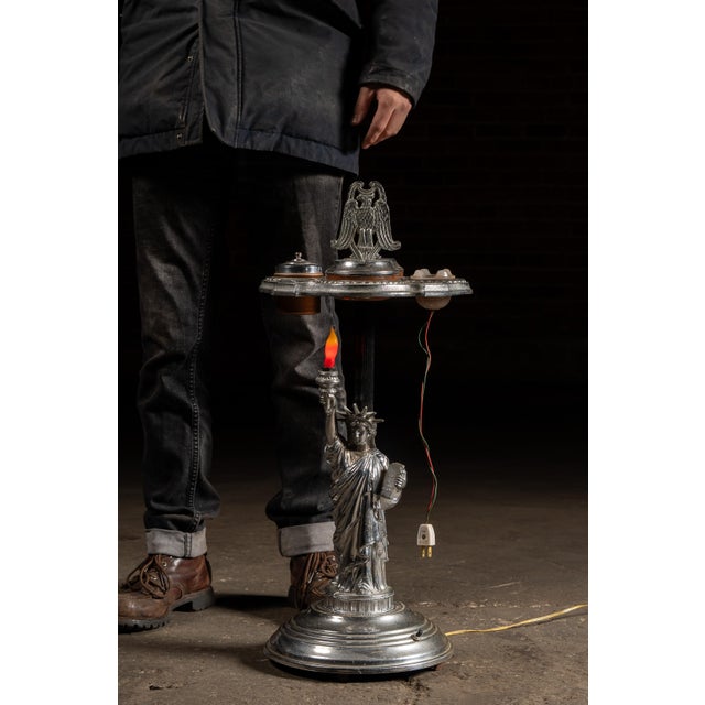 Cast metal smoking stand centered by a figural Statue of Liberty form, her raised torch converted into a glowing electric...