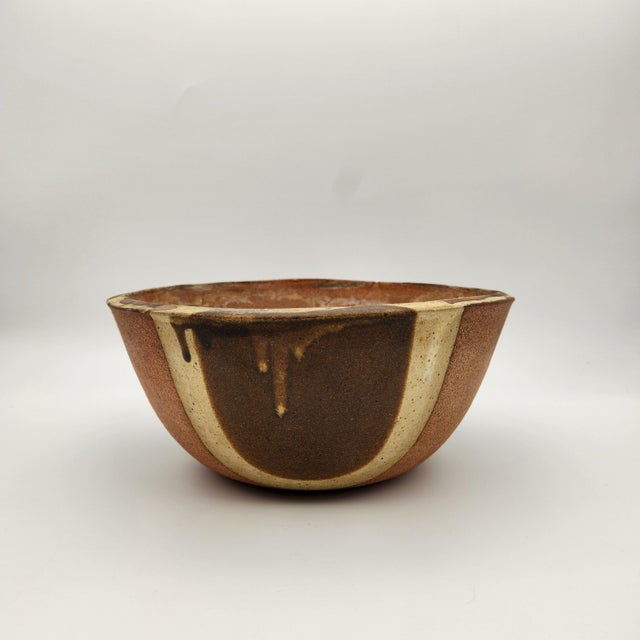 Hand-thrown stoneware bowl with bold vertical stripe pattern in earth tones of rust, brown, and cream with drip glaze...