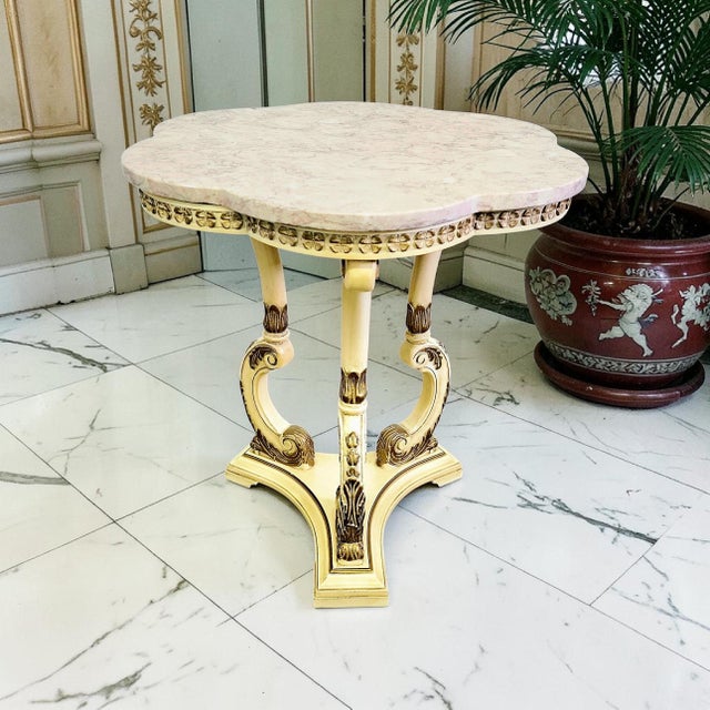 Vintage Hollywood Regency side table featuring a shaped pink marble top over an ornate gilt pedestal base with...