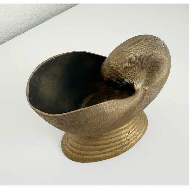 1970s Tony Duquette-style solid brass pedestal bowl. The planter bowl features a nautilus-shaped vessel fixed atop a...