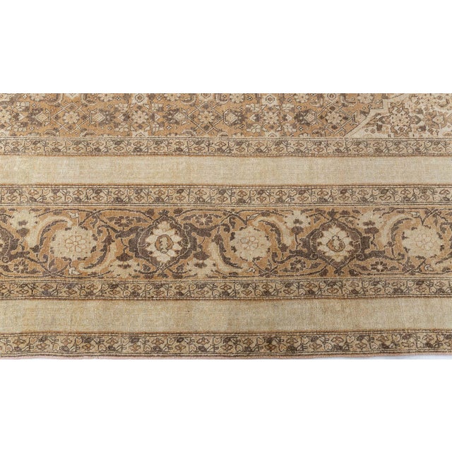 An early 20th century Persian Antique Tabriz rug, the cream field with rows of staggered finely-drawn botehs around...