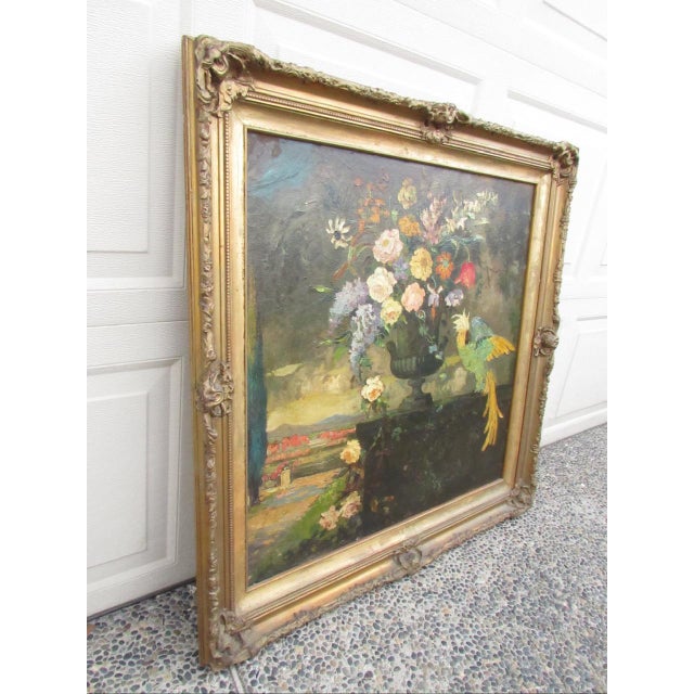 A vibrant floral still life oil on board painting of a bouquet of flowers in an urn on a terrace and overseen by a...