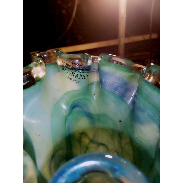 This rippled glass vase has streaks of blue and dark green on a pale green color field. It contains a maker's label for...