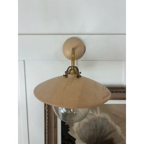 Wall-mounted sconce featuring a circular wood shade with a clear glass globe suspended beneath. The shade is flat and...