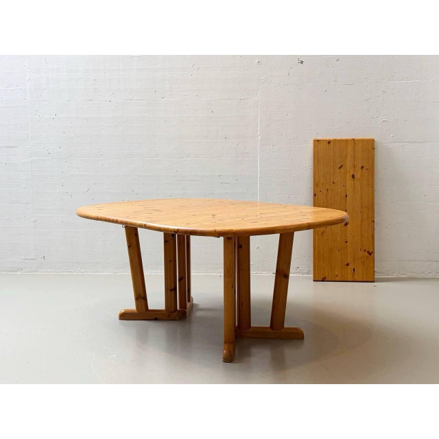 A generously sized, extendable dining table in a rustic, functional design with a clean, understated aesthetic. The...