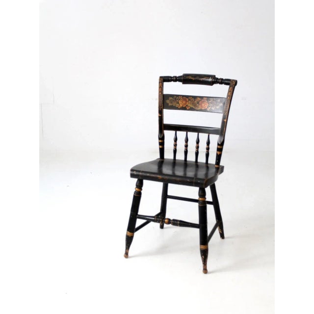 A vintage L. Hitchcock chair finished in classic black with hand-applied golden stencil work across the crest and back...