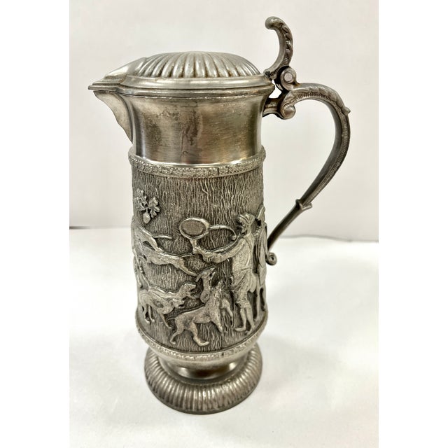 Vintage pewter pitcher. Heavily embossed hunting scene encircles this tankard. Decorative curved handle. The pitcher...