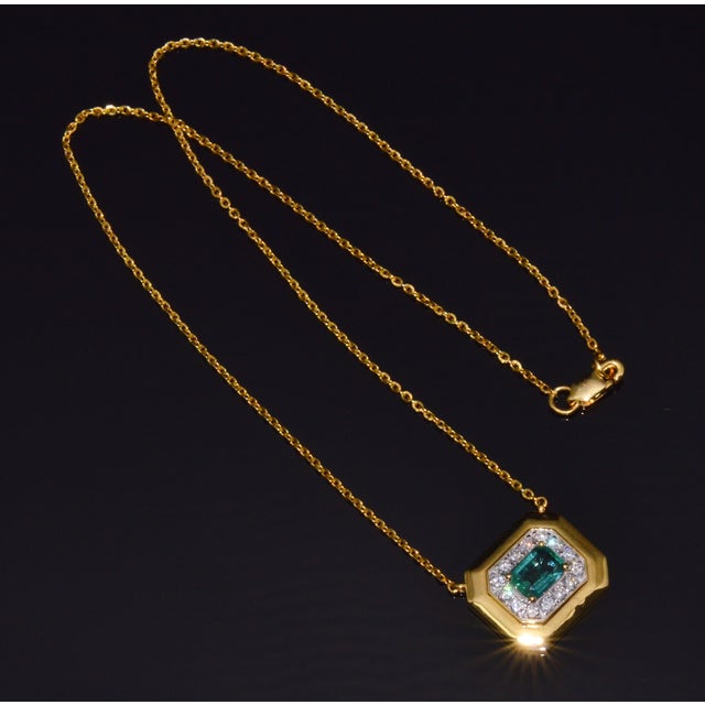 This necklace features a luxurious domed halo design centered around a vibrant natural octagonal step cut emerald weighing...