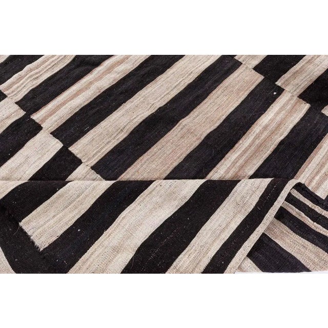 A mid-century Persian Kilim rug from the 1950s, woven in a striking black and ivory palette. The minimalist design...