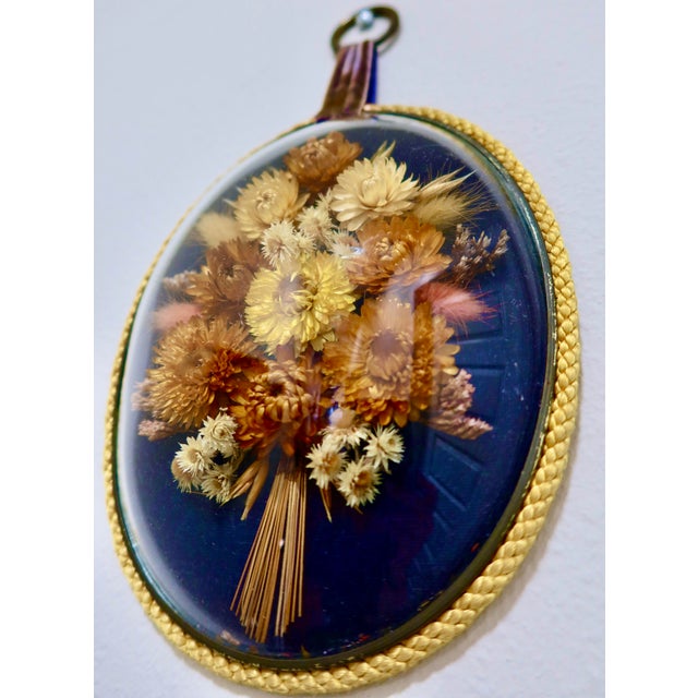 A beautifully preserved oval dried flower arrangement displayed beneath convex glass in a gilt braided frame with a velvet...