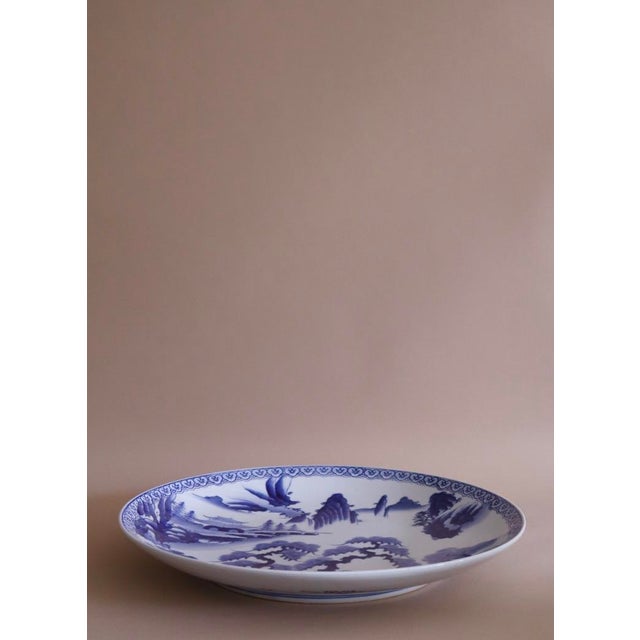 Oversized antique hand-painted blue and white plate from China depicting outdoor landscape.