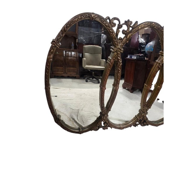 An impressive vintage Hollywood Regency triple wall mirror featuring three elegant oval mirrors framed by an elaborately...