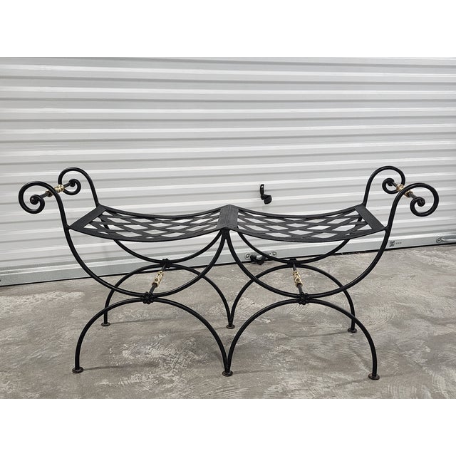 Mid century Neoclassical inspired black painted wrought iron bench, with woven seat metal strapwork and brass accents. A...