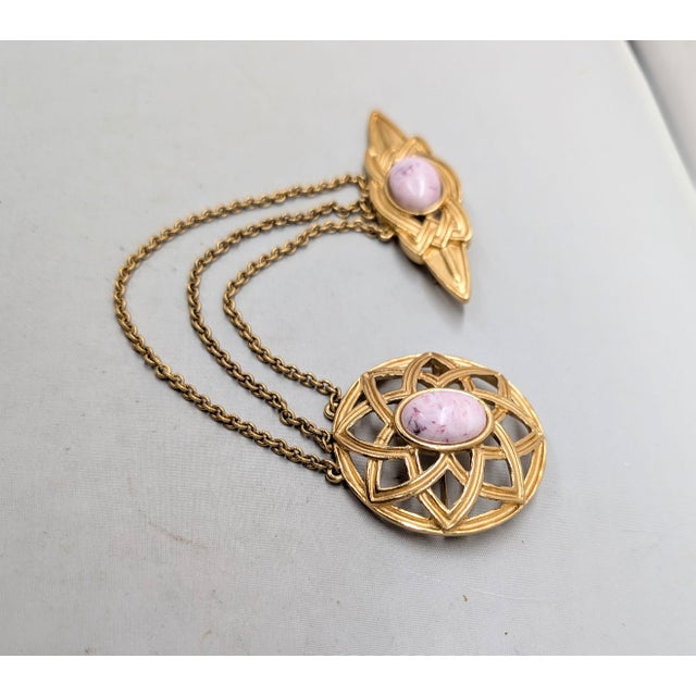 1980s goldtone round openwork with oval pink marbled cabochon rhinestone center with 3 chains connecting to a celtic knot...
