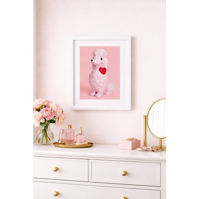 A pink ceramic poodle with a red heart is photographed against a soft pink background, creating a playful monochrome still...