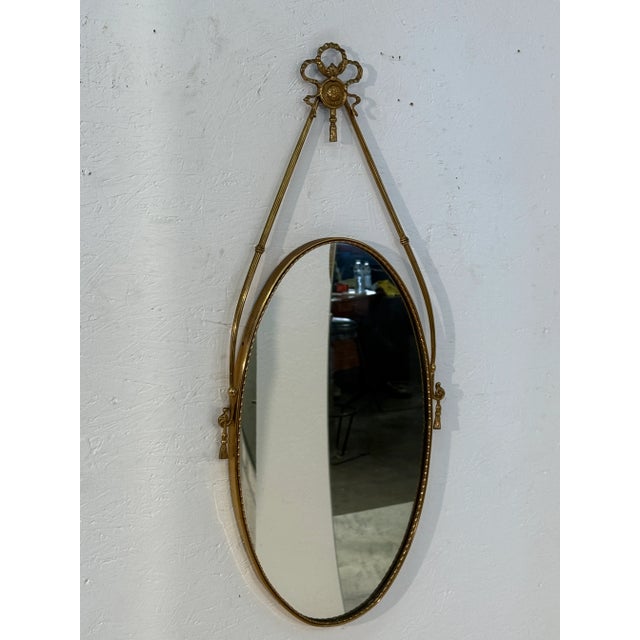 Italian oval mirror dating to the 1950s, framed in gilt brass with neoclassical-inspired ornamentation. The design...