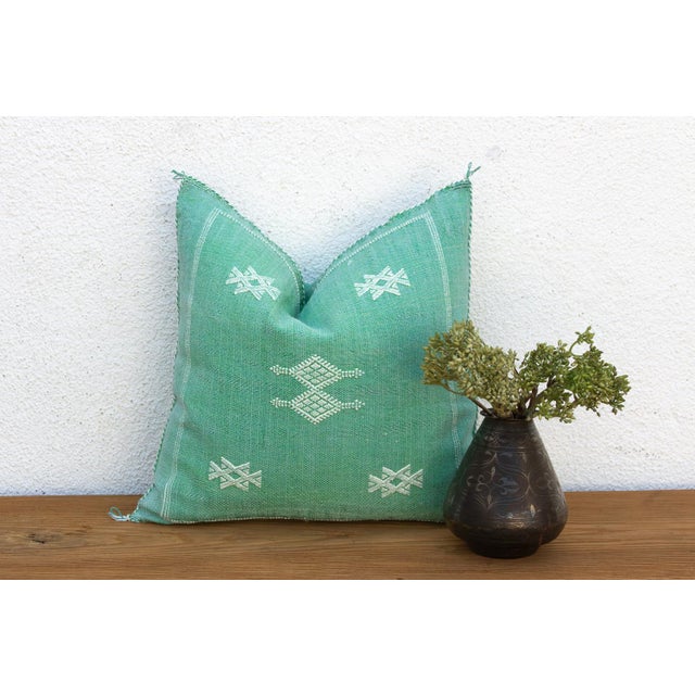A single star motif and a slim dashed-line border trace the corner of this handcrafted Moroccan cactus silk pillow, hand-...