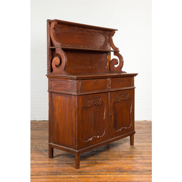 An antique Indonesian dining display cabinet from the early 20th century, with two drawers and two doors with carved...