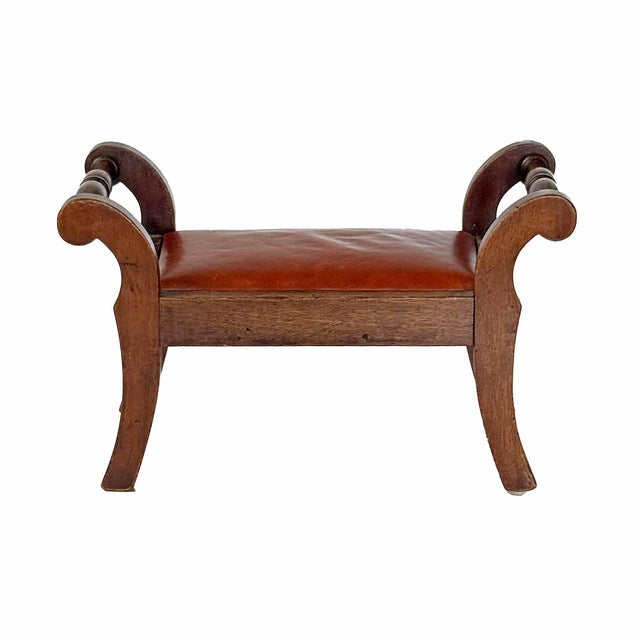Antique Empire period footstool or small bench featuring a mahogany frame, scroll arms, and a leather seat. Repair near...