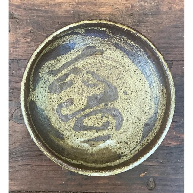This pottery plate presents a shallow, rounded form with gently curving sides that rise from a wide central well to a...